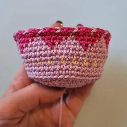 Close-up of pink crocheted flower pot with heart-pattern colorwork around the side