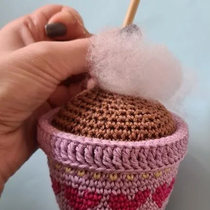 Polyester fiberfill being added to the crocheted brown soil inside the flower pot