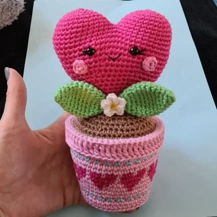 Finished pink crochet heart plant in a pink pot with green leaves and tiny white flower