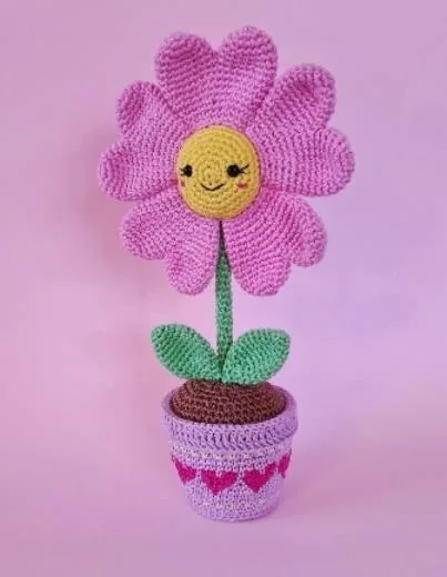Finished pink daisy crochet flower with yellow smiling face, green leaves and pink flower pot