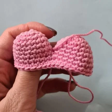 Two pink crocheted rounded tops being joined to form a heart-shaped daisy petal