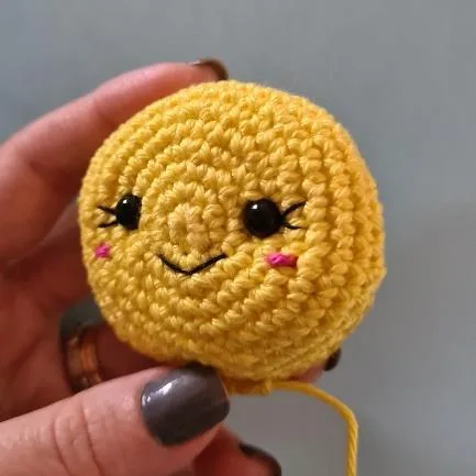 Yellow crocheted flower center with stitched smile, eyelashes and safety eyes